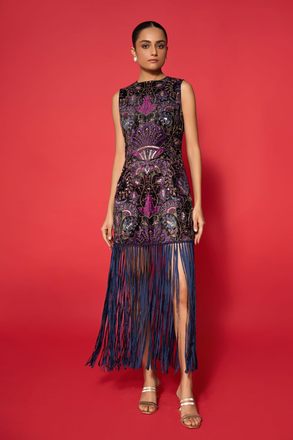 Woman wearing a sleeveless dress with intricate patterns and fringes on a red background