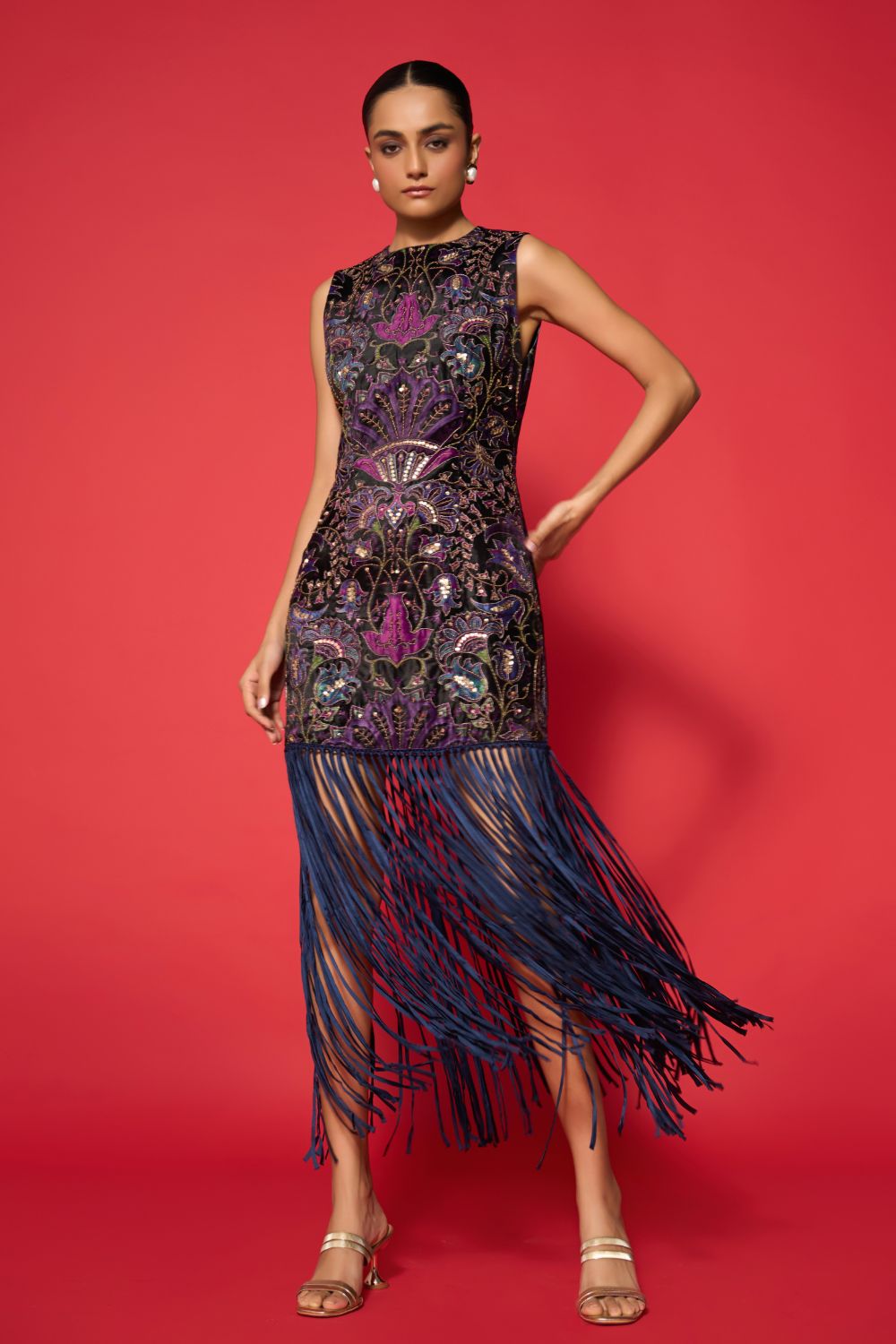 Woman wearing a sleeveless dress with intricate patterns and fringes on a red background