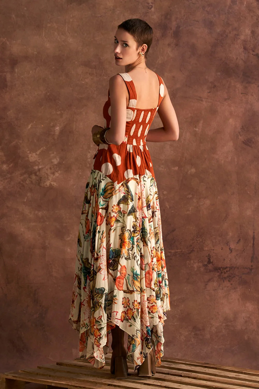Woman wearing a colorful dress with a patterned back against a brown textured wall.