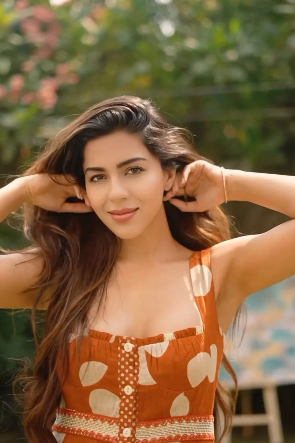 Woman with long hair wearing an orange dress with white patterns outdoors.