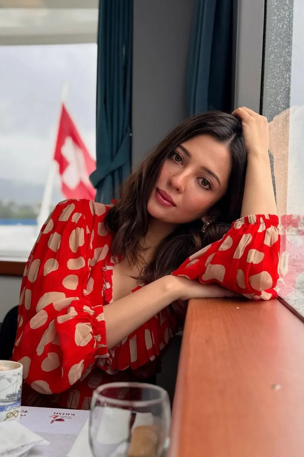 Woman in a red polka dot dress sitting at a table with a scenic view outside.