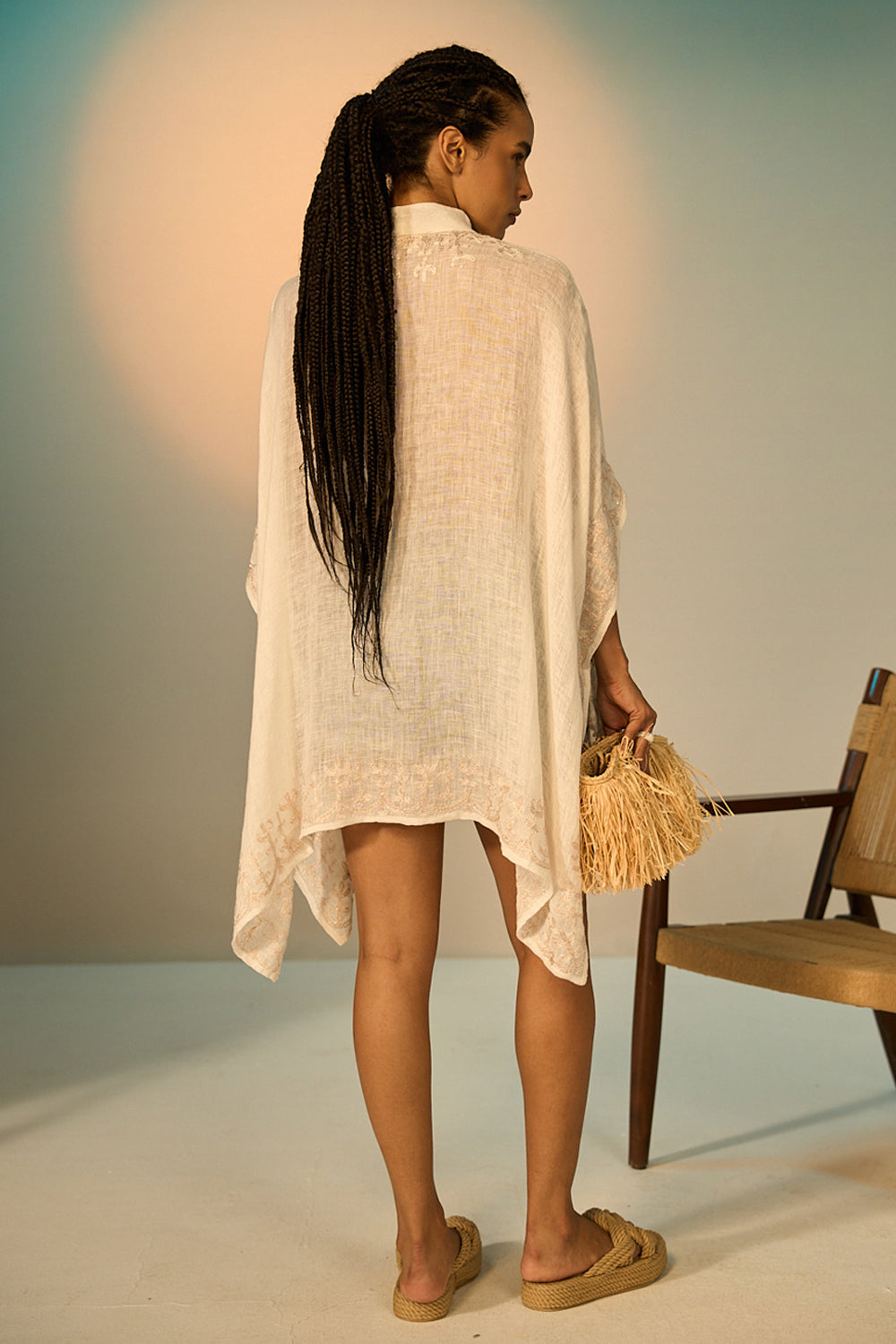 Woman in a light-colored dress holding a basket, standing against a neutral background.