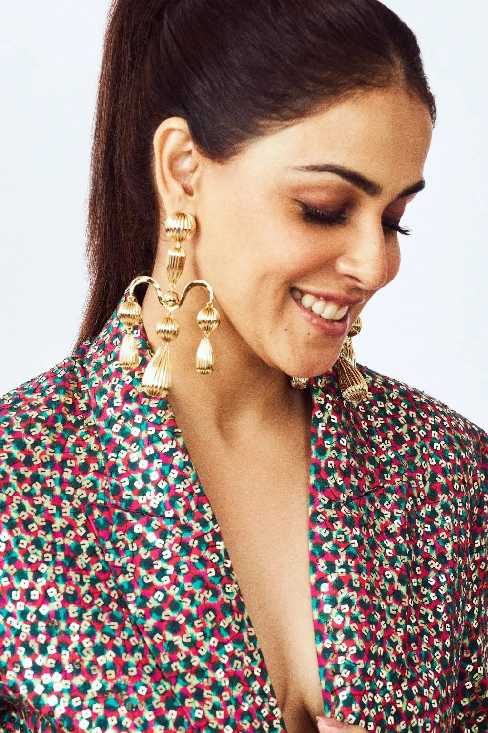 Woman wearing gold earrings with a colorful top against a white background