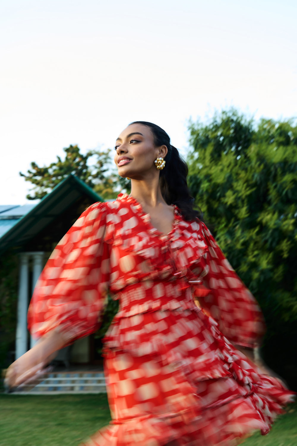 Woman in a red and white patterned dress standing outdoors with greenery in the background