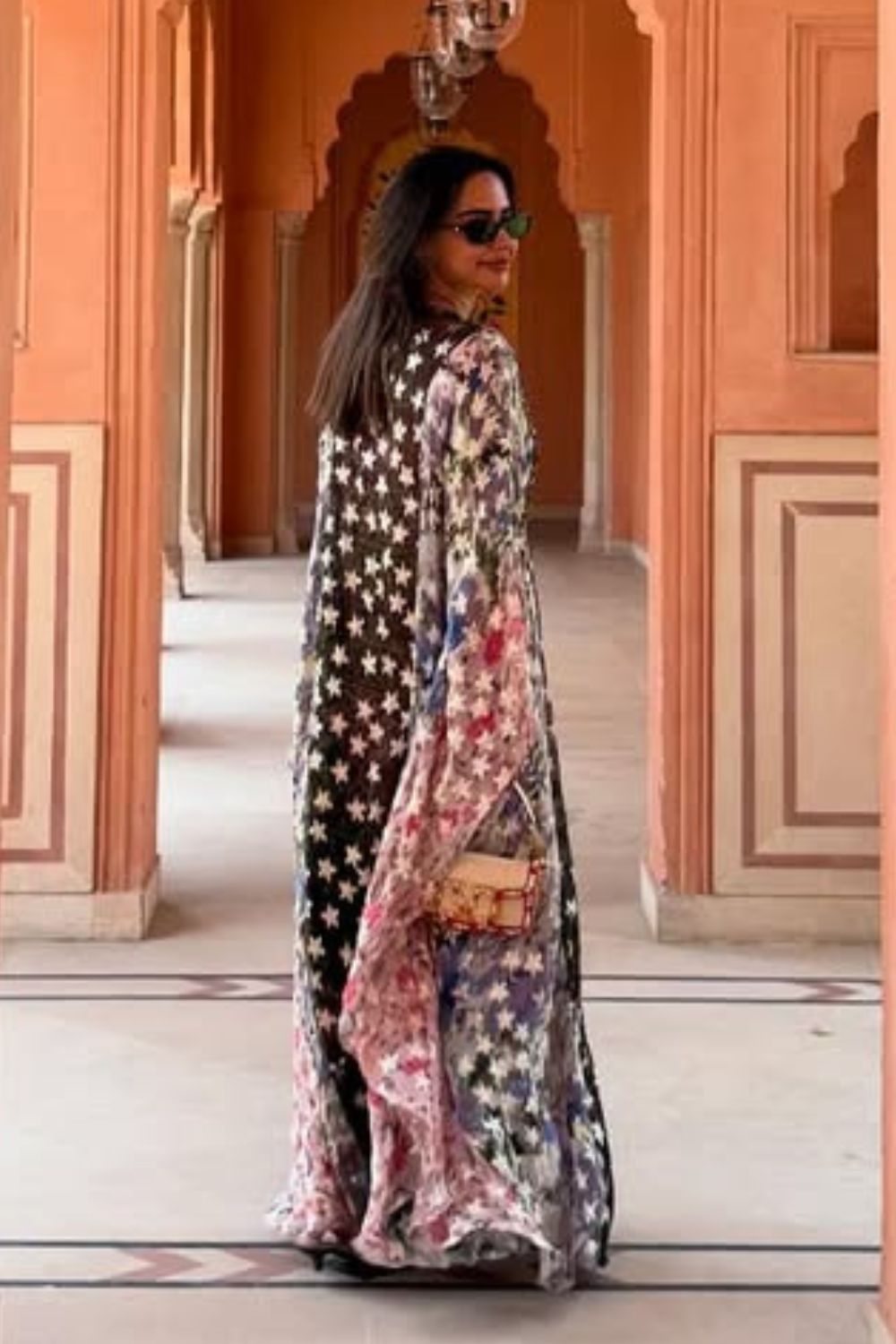 Woman in a floral dress standing in an architectural setting with arched doorways.