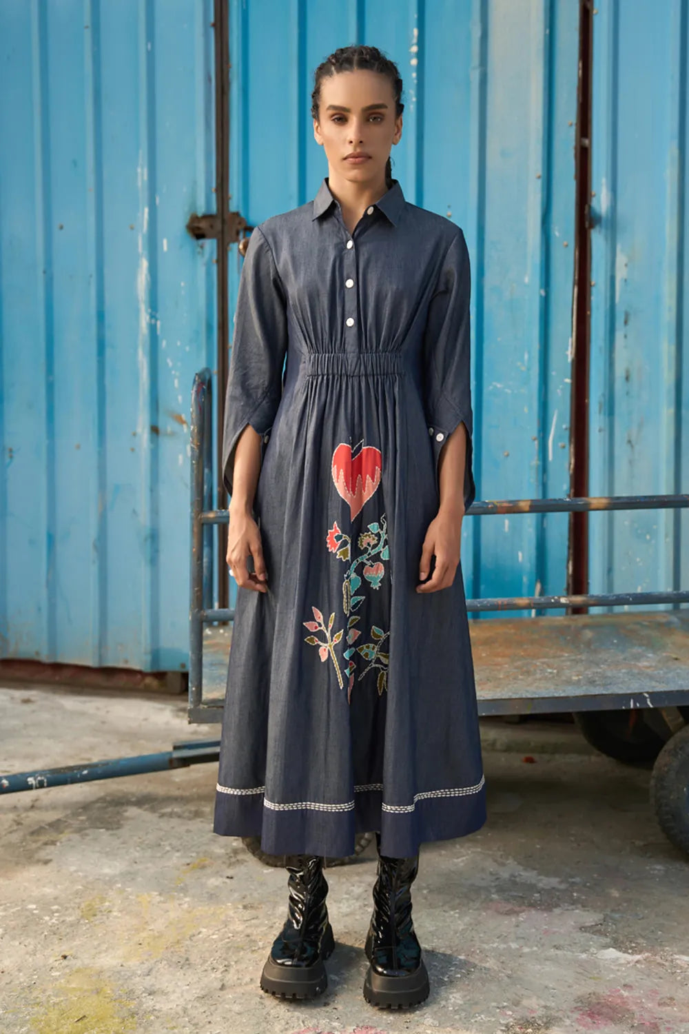 Maria Embroidered Maxi Dress women's dark blue chambray midi shirt dress featuring a collared neckline, button-down front, elasticated ruched waist, slightly flared sleeves and a bold embroidered heart with floral detailing, finished with contrast stitching, styled for summer brunches, casual dinners and day-to-evening outings.