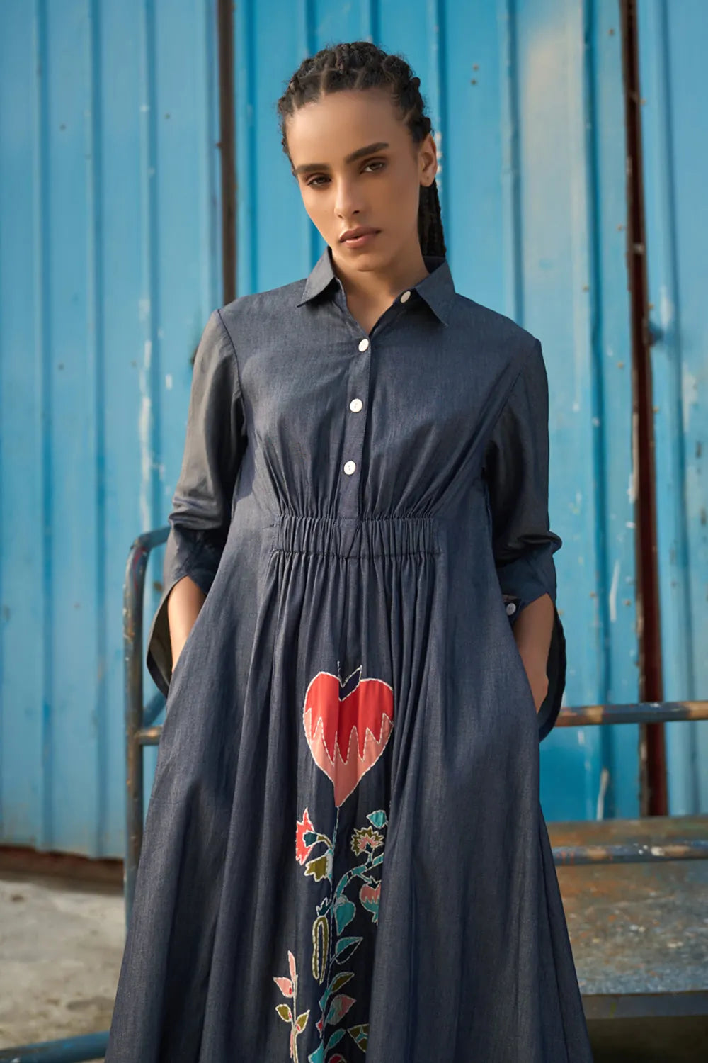 Maria Embroidered Maxi Dress women's dark blue chambray midi shirt dress featuring a collared neckline, button-down front, elasticated ruched waist, slightly flared sleeves and a bold embroidered heart with floral detailing, finished with contrast stitching, styled for summer brunches, casual dinners and day-to-evening outings.