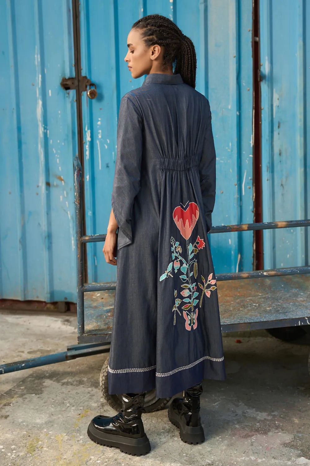 Maria Embroidered Maxi Dress women's dark blue chambray midi shirt dress featuring a collared neckline, button-down front, elasticated ruched waist, slightly flared sleeves and a bold embroidered heart with floral detailing, finished with contrast stitching, styled for summer brunches, casual dinners and day-to-evening outings.