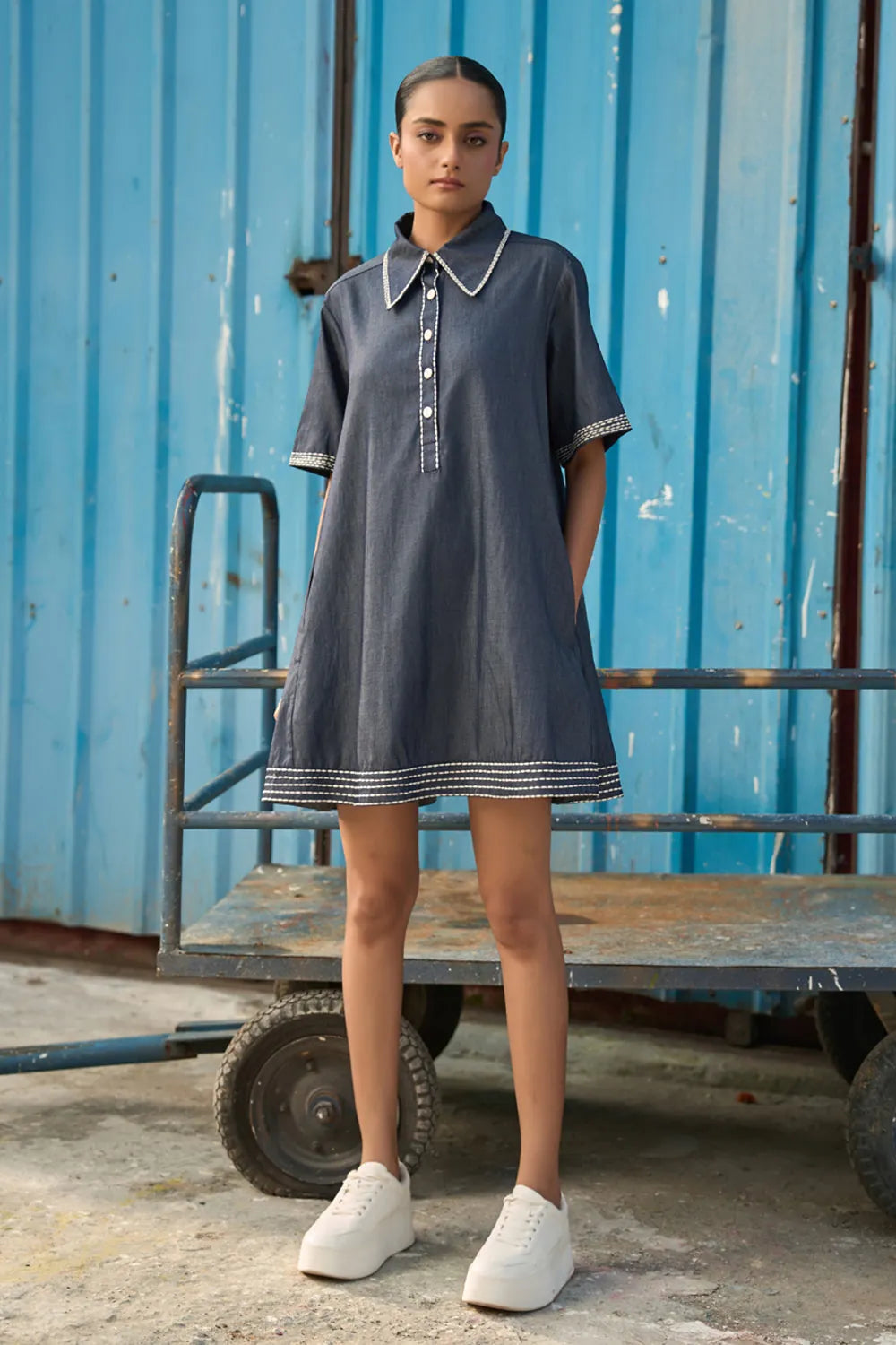 Rico Mini Dress women's dark blue chambray mini dress featuring a sharp pointed collar, short sleeves, a partial button-down front and contrast white stitching along the collar, sleeves, button placket and hem, finished with a loose flared A-line silhouette for casual outings, summer travel, relaxed daytime wear and casual dinners.