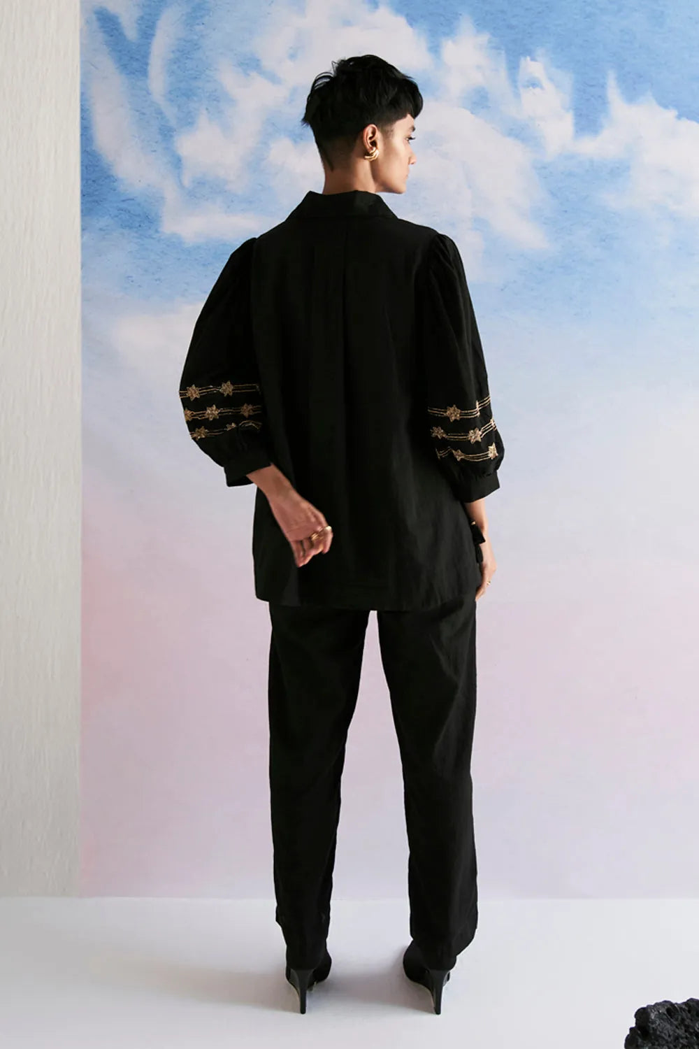 Back view of Rimi Co-ord Set women's black cotton outfit featuring a coordinated relaxed shirt and tailored pants, a long shirt silhouette and clean contemporary styling, designed for comfortable travel, elevated daywear, casual gatherings and sophisticated everyday dressing.