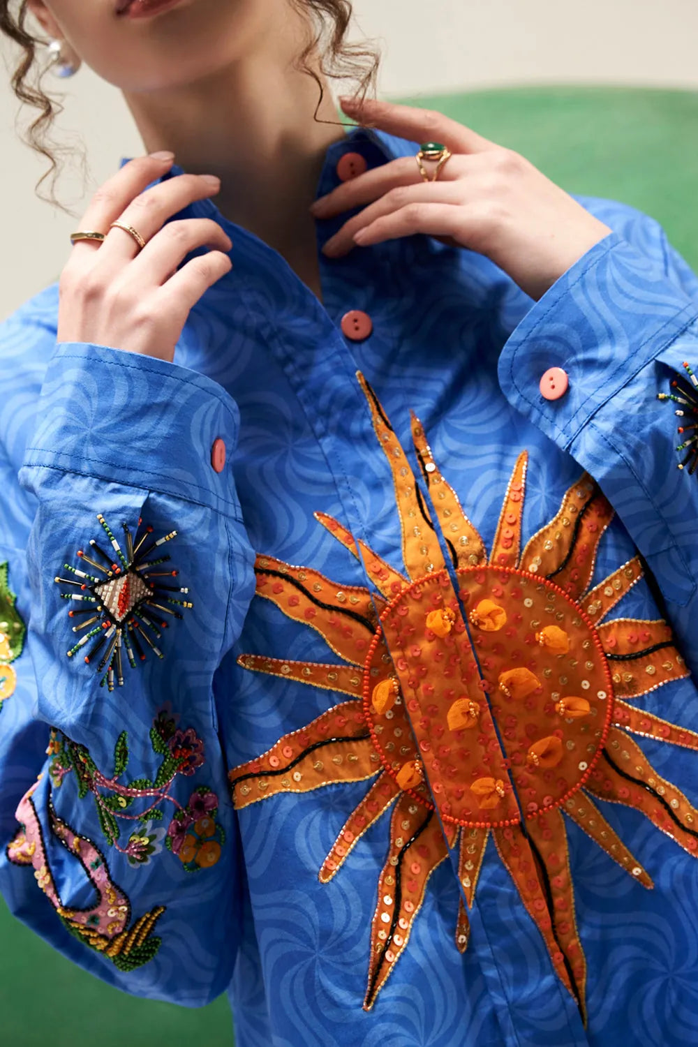 Close-up of Arin cobalt blue shirt showing the embroidered orange sun motif, colourful sleeve embroidery and button-down collar detail