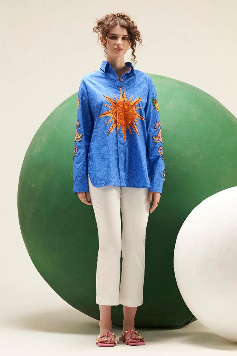 Arin cobalt blue cotton shirt with relaxed fit, long sleeves and embroidered orange sun motif styled with white trousers
