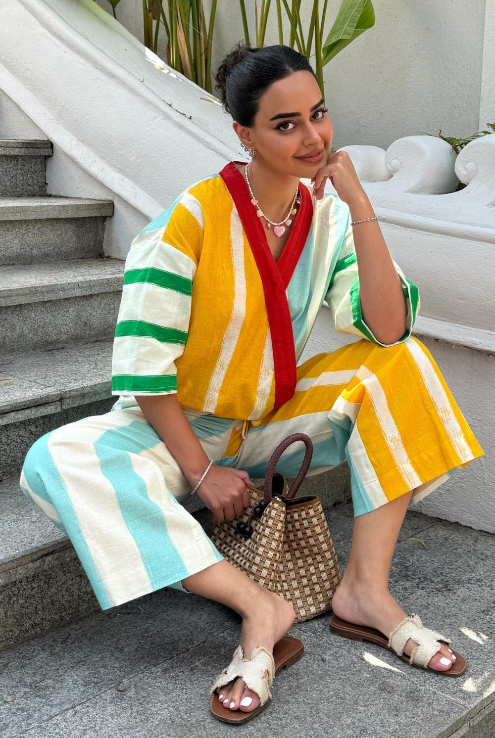 Arushi Mehra in a colorful striped outfit sitting in an outdoor setting with plants and a white wall.
