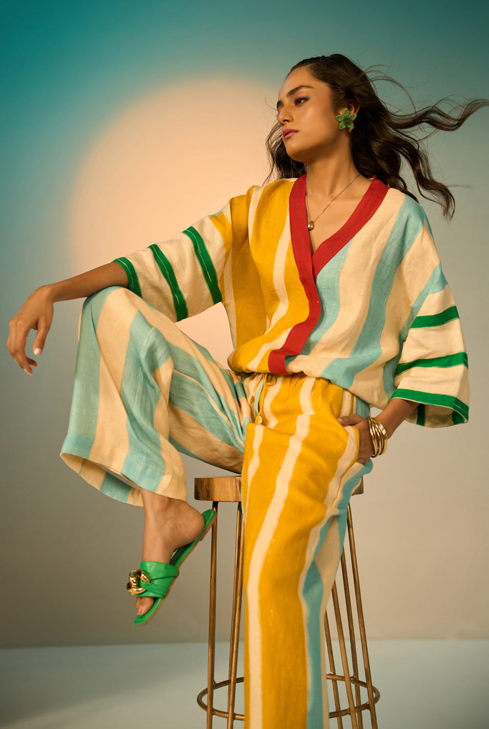 Woman in a colorful striped outfit sitting on a stool with a gradient background