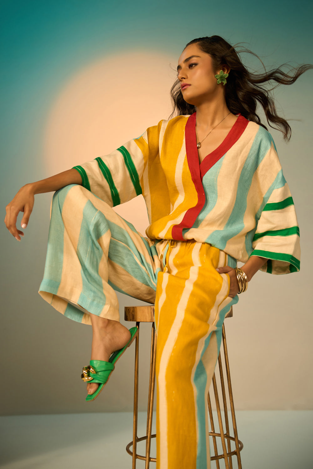 Woman in a colorful striped outfit sitting on a stool with a gradient background