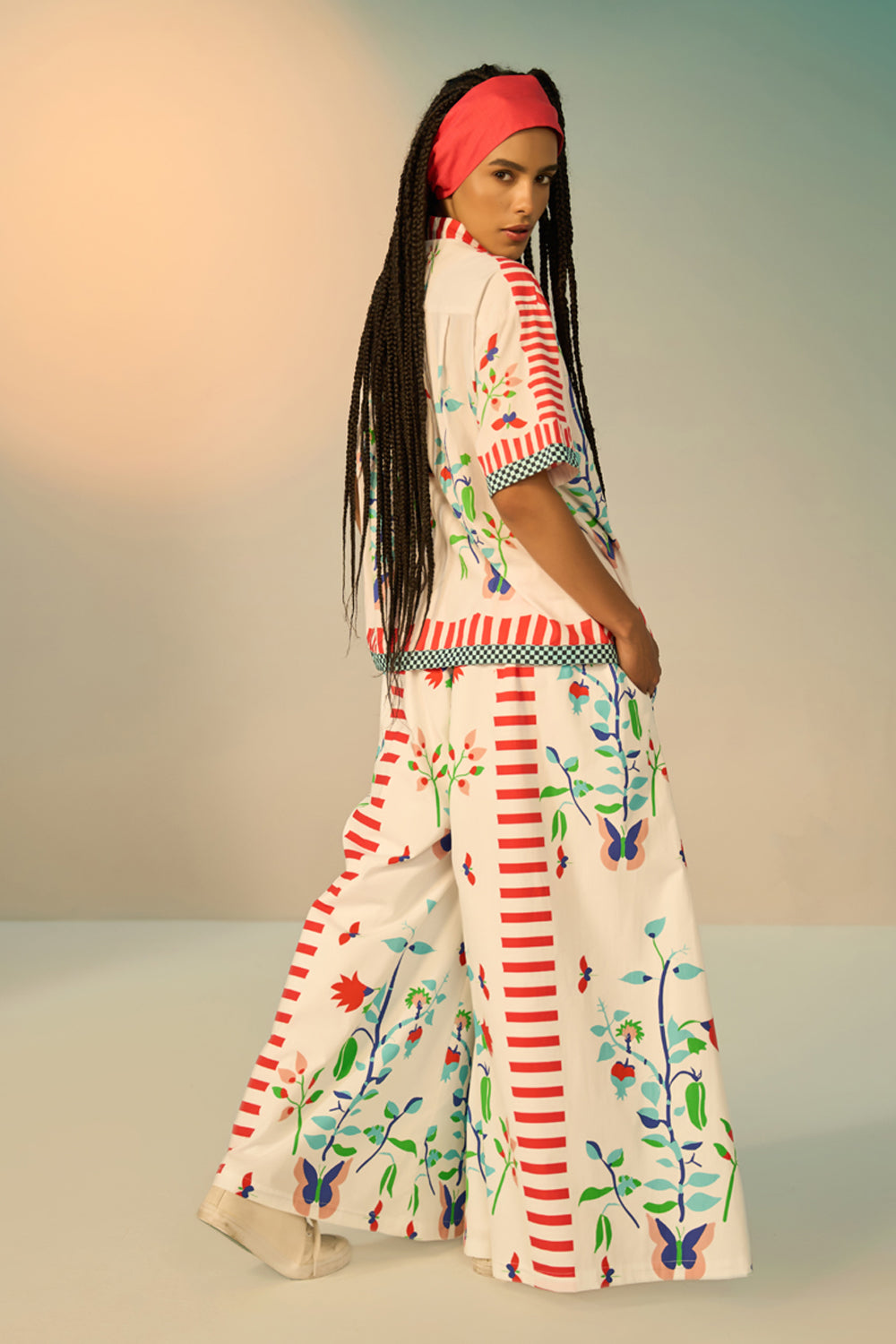 Woman wearing a ivory outfit set with a patterned shirt and pants on a plain background