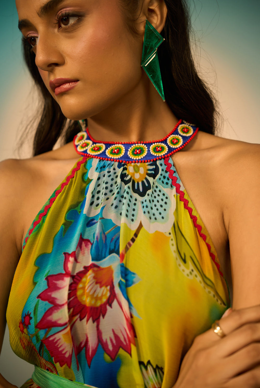 Close-up look of a woman modeling a sleeveless halter-neck midi dress with a vibrant multicolor floral and abstract print in shades of blue, green, yellow, and pink, styled with lime green pointed-toe heels against a studio backdrop.