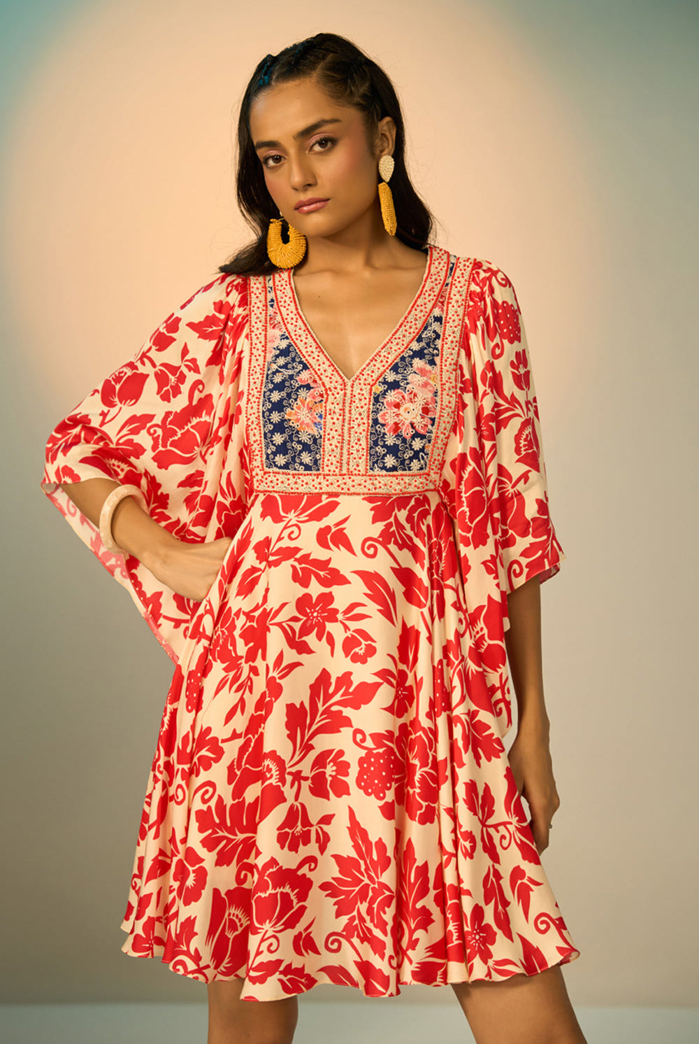 A woman modeling a embroidered tunic with a red floral print on a cream background, featuring a navy blue embroidered yoke with redfloral details and a geometric border.