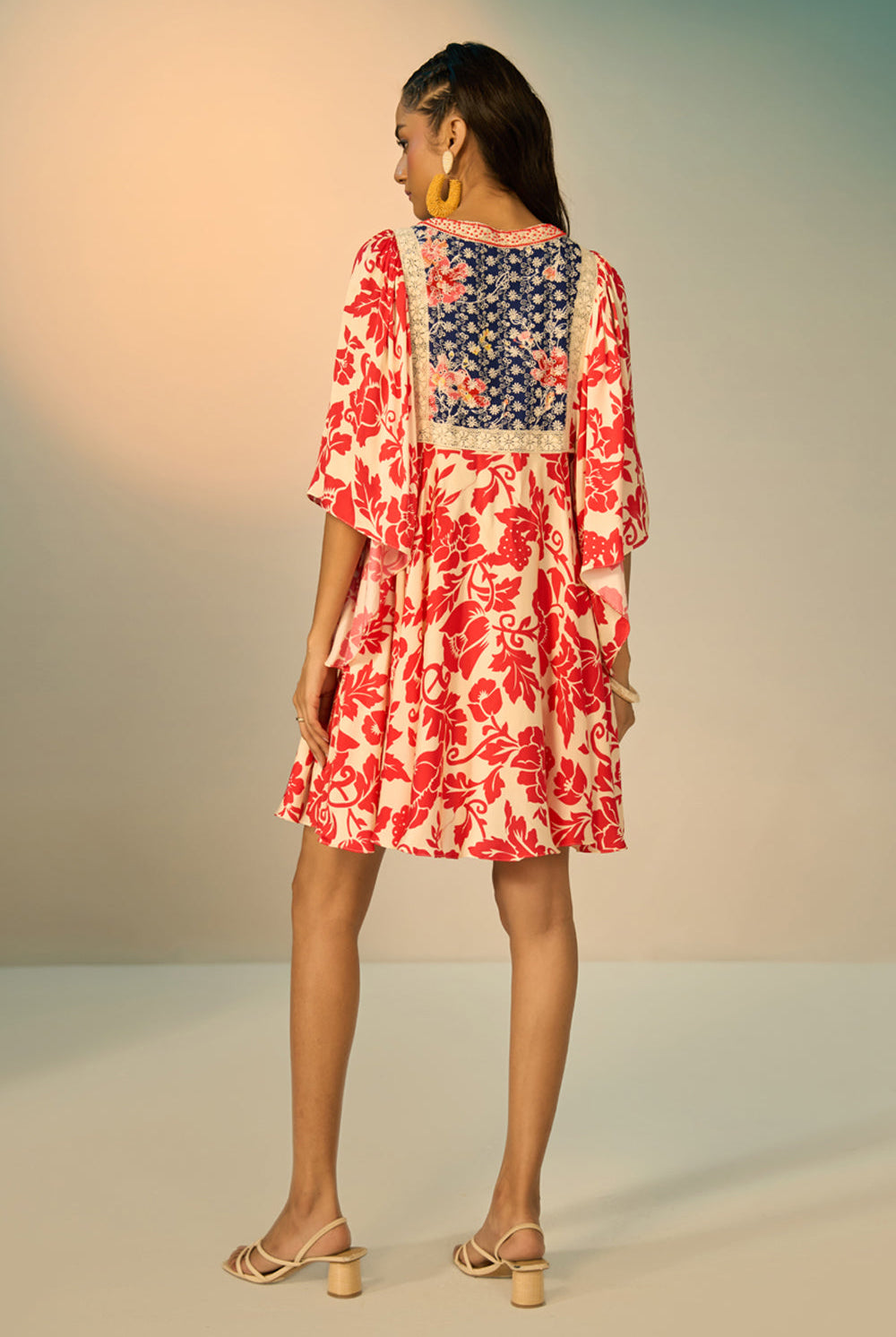 A woman modeling a embroidered tunic with a red floral print on a cream background, featuring a navy blue embroidered yoke with redfloral details and a geometric border.