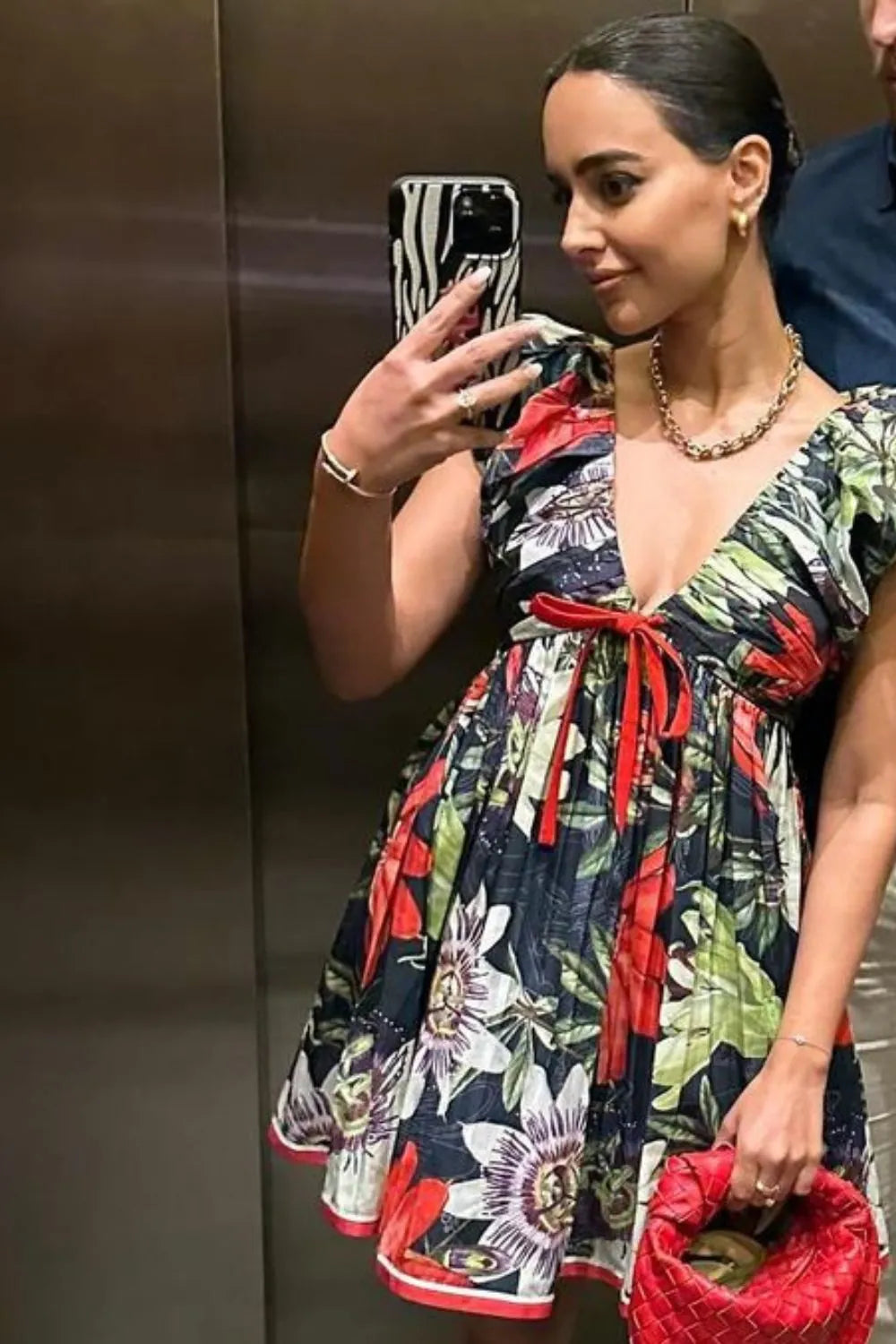 Woman taking a mirror selfie wearing a colorful floral dress in an elevator.