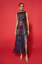 Woman wearing a sleeveless dress with intricate patterns and fringes on a red background