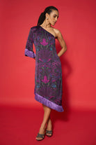 Woman wearing a purple one-shoulder dress with intricate patterns against a red background