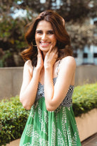 Woman in a green dress with a checkered top, posing outdoors.