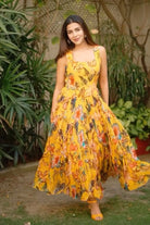 Woman wearing a yellow floral dress standing outdoors with greenery in the background