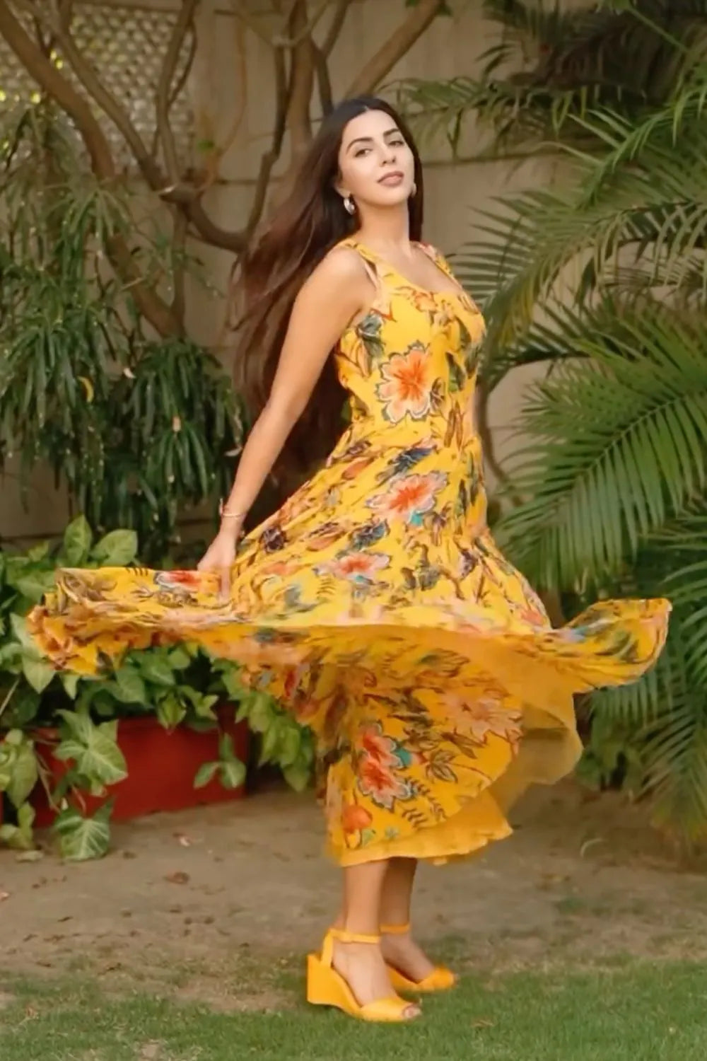 Woman in a yellow floral dress standing outdoors with greenery around
