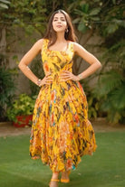 Woman in a yellow floral dress standing outdoors with greenery in the background