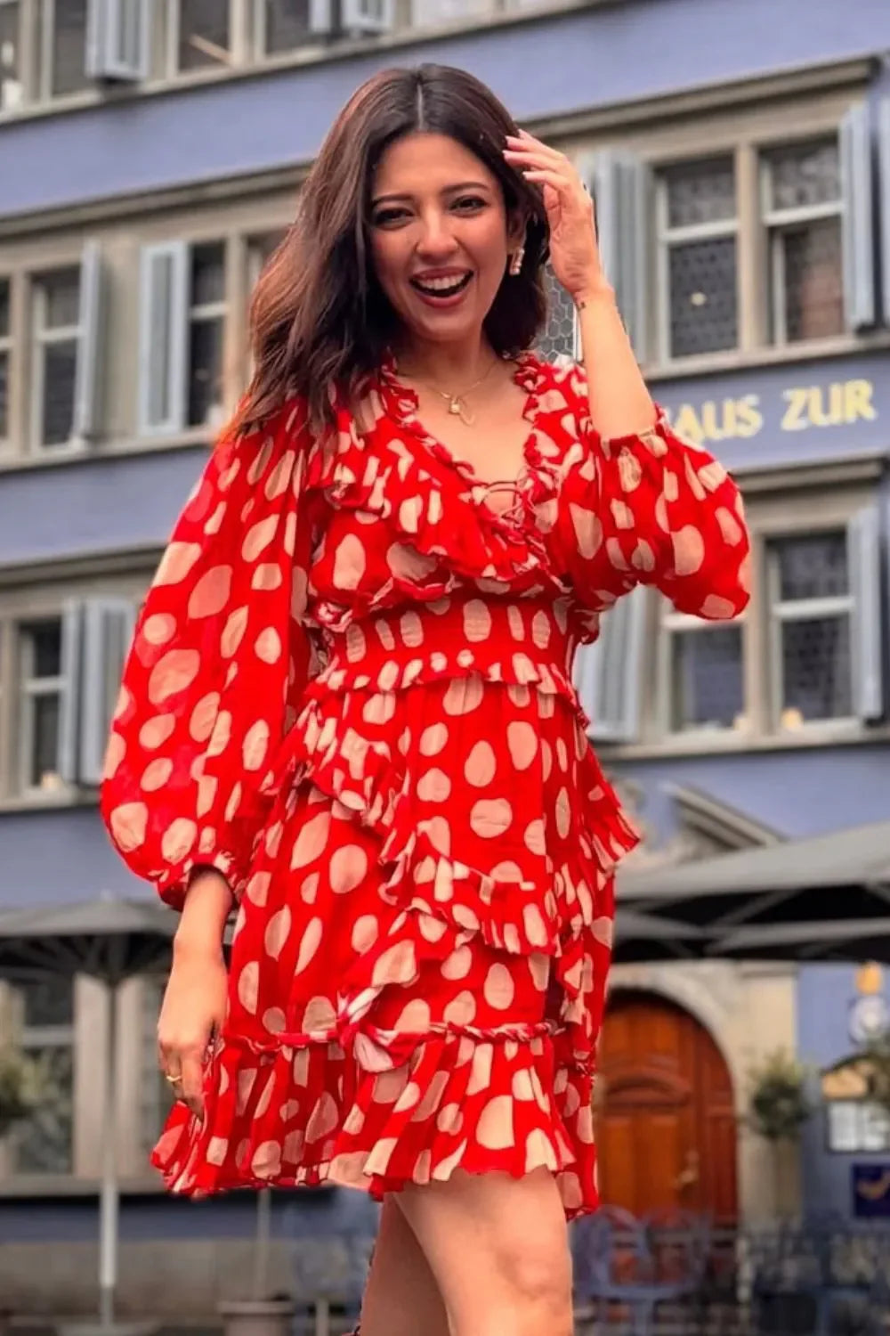 Woman wearing a red polka dot dress standing in front of a building with a sign.