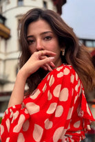 Woman wearing a red dress with white polka dots, posing outdoors.