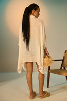 Woman in a light-colored dress holding a basket, standing against a neutral background.
