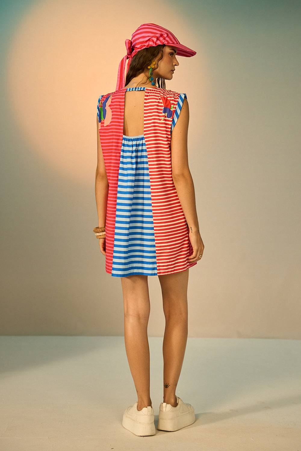 Woman wearing a red and blue striped dress with a matching hat against a neutral background
