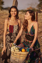 Two women in patterned dresses standing outdoors with a basket of flowers.