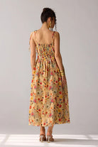 Back view of Dixie Dress women's beige chiffon maxi dress featuring a corset-fitted bodice, an elegant flowing skirt and an adjustable smocked back for a flattering fit, styled for summer getaways, resort dinners, luncheons and special occasions.