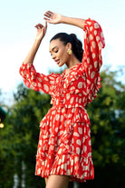 Woman in a red dress with white polka dots posing outdoors.