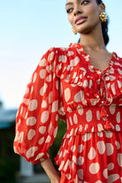 Closeup look of Izia Dress women's coral red Viscose Georgette mini dress featuring a playful white polka dot print, a tie-up neckline with beaded tassels and delicate ruffle detailing, styled for summer brunches, beach holidays, vacation outings and casual daytime gatherings.