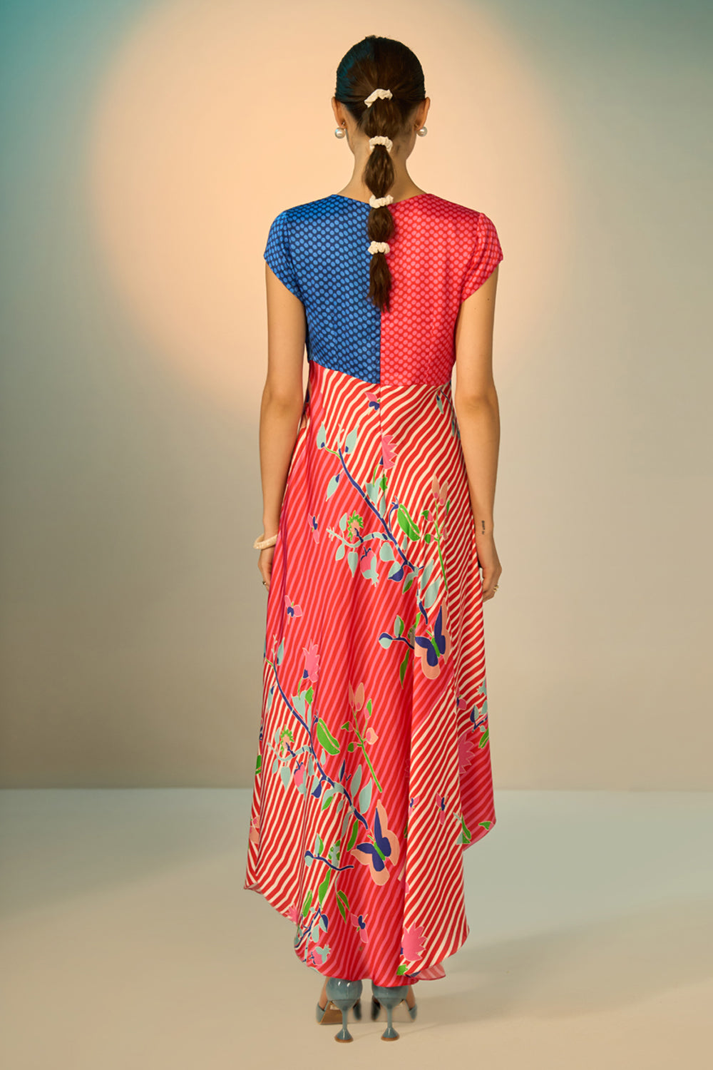 Woman wearing a colorful dress with a blue top and red skirt, standing against a plain background.