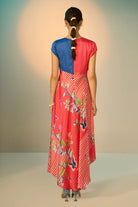 Woman wearing a colorful dress with a blue top and red skirt, standing against a plain background.