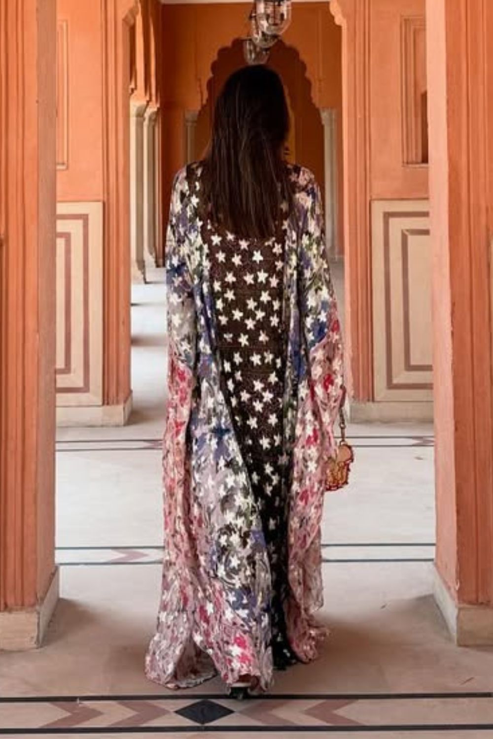 Woman in a long, patterned dress standing in an ornate hallway.