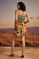 Back view of Lilly Mini Dress in Sunny Mustard women's mustard yellow viscose georgette mini dress featuring a vibrant floral print and a playful, lightweight silhouette, styled for summer brunches, vacation outings, garden parties and resort holidays.