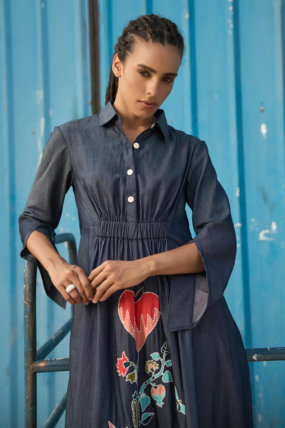 Maria Embroidered Maxi Dress women's dark blue chambray midi shirt dress featuring a collared neckline, button-down front, elasticated ruched waist, slightly flared sleeves and a bold embroidered heart with floral detailing, finished with contrast stitching, styled for summer brunches, casual dinners and day-to-evening outings.