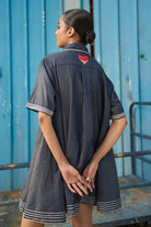 Back view of Rico Mini Dress women's dark blue chambray mini dress featuring a sharp pointed collar, short sleeves, a partial button-down front and contrast white stitching along the collar, sleeves, button placket and hem, finished with a loose flared A-line silhouette for casual outings, summer travel, relaxed daytime wear and casual dinners.