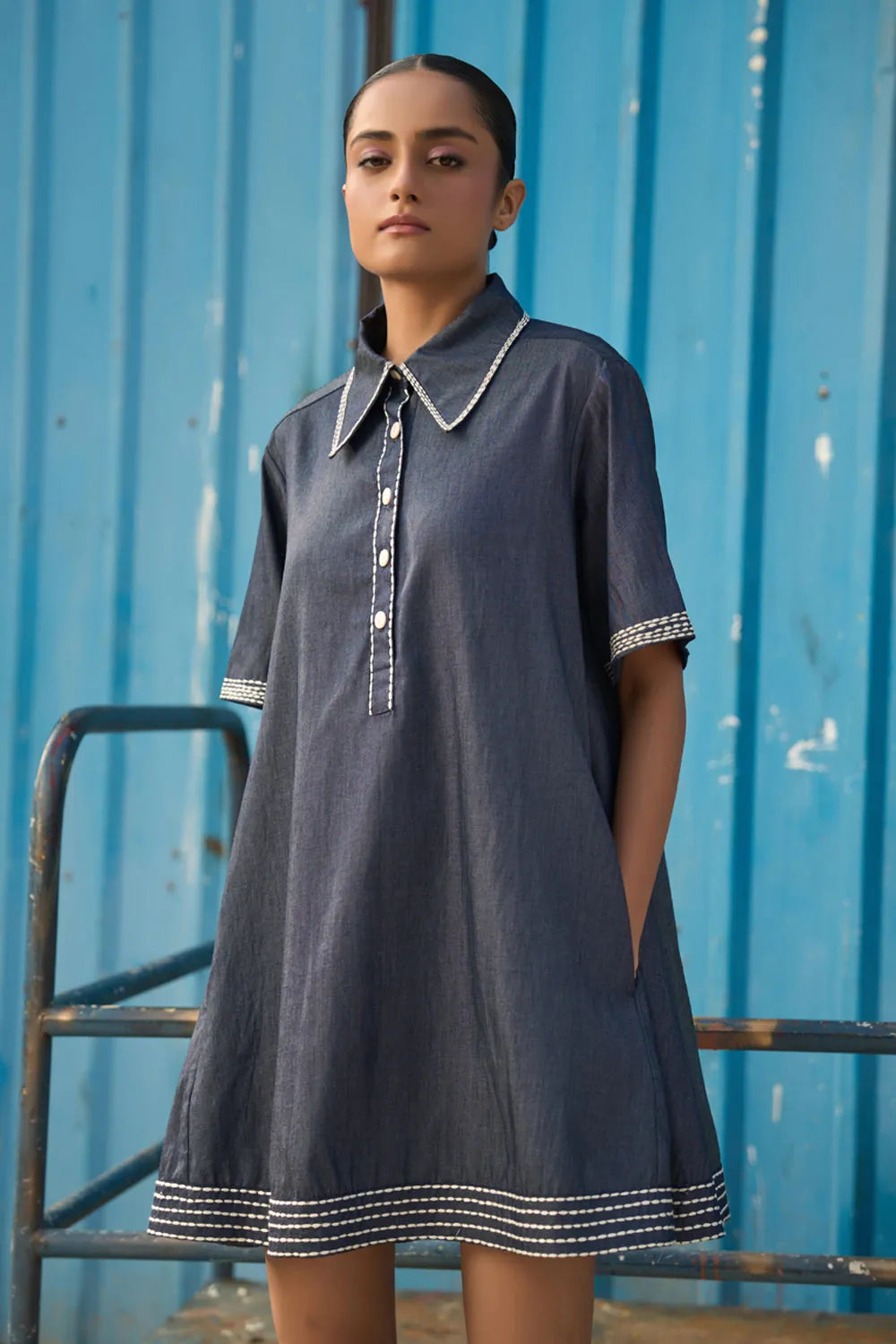 Full view of Rico Mini Dress women's dark blue chambray mini dress featuring a sharp pointed collar, short sleeves, a partial button-down front and contrast white stitching along the collar, sleeves, button placket and hem, finished with a loose flared A-line silhouette for casual outings, summer travel, relaxed daytime wear and casual dinners.