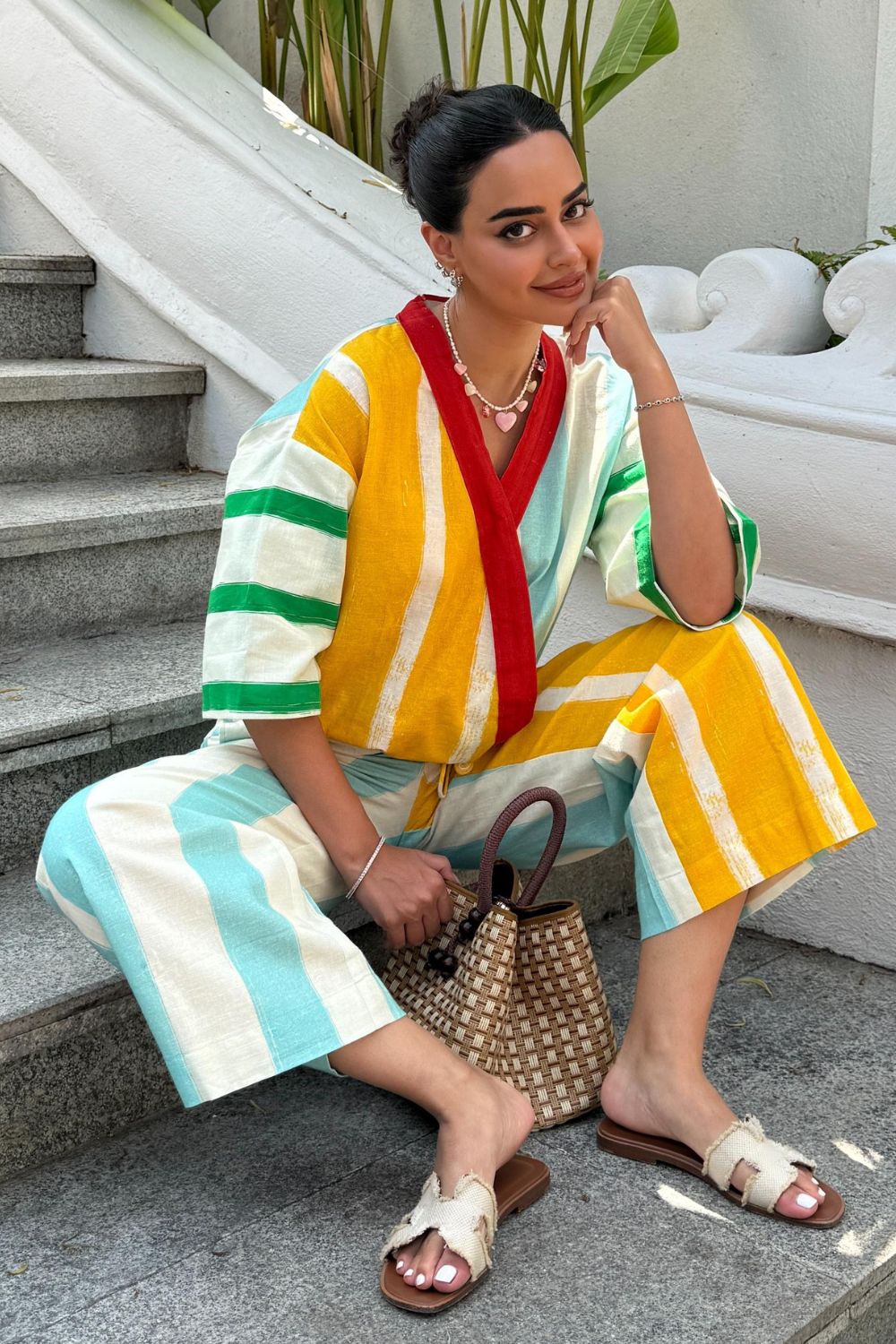 Arushi Mehra in a colorful striped outfit sitting in an outdoor setting with plants and a white wall.