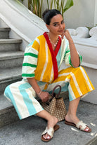 Arushi Mehra in a colorful striped outfit sitting in an outdoor setting with plants and a white wall.