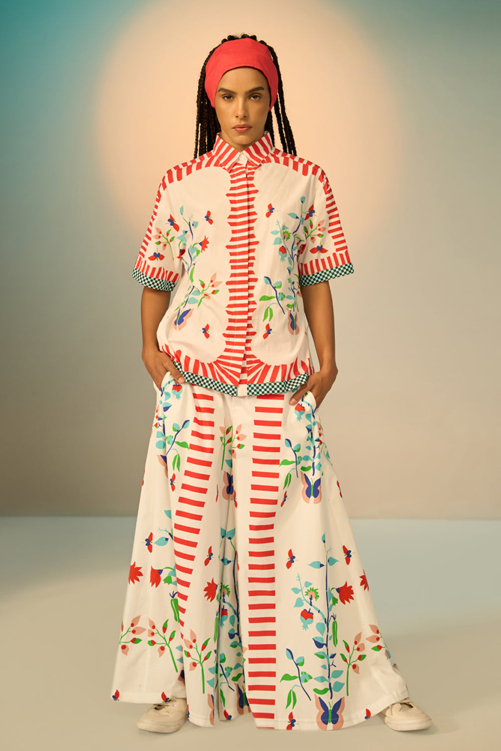 Woman wearing a ivory outfit set with a patterned shirt and pants on a plain background