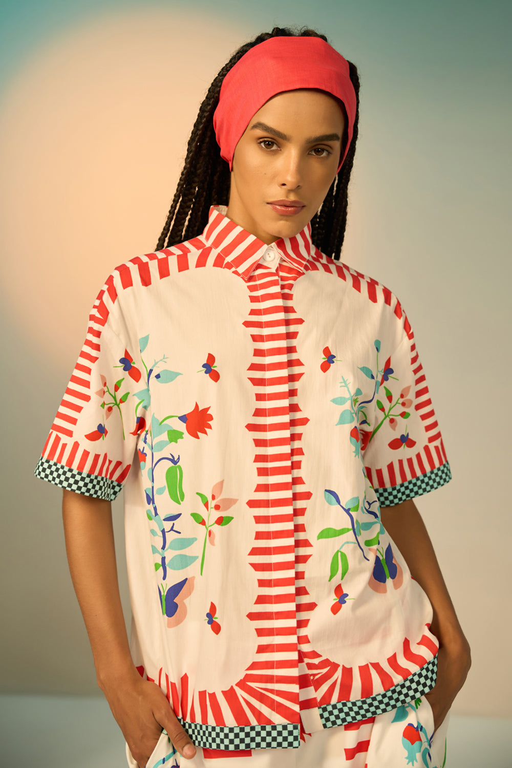 Woman wearing a ivory outfit set with a patterned shirt and pants on a plain background