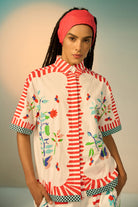 Woman wearing a ivory outfit set with a patterned shirt and pants on a plain background